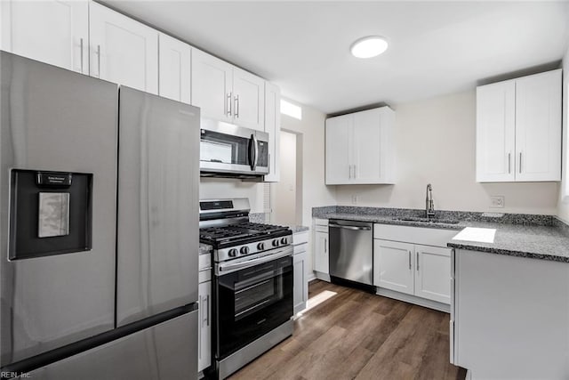 kitchen with appliances with stainless steel finishes, dark wood-type flooring, white cabinets, stone countertops, and sink