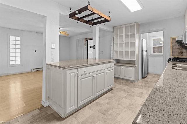 kitchen with white cabinetry, light stone counters, tasteful backsplash, stainless steel fridge, and a baseboard radiator