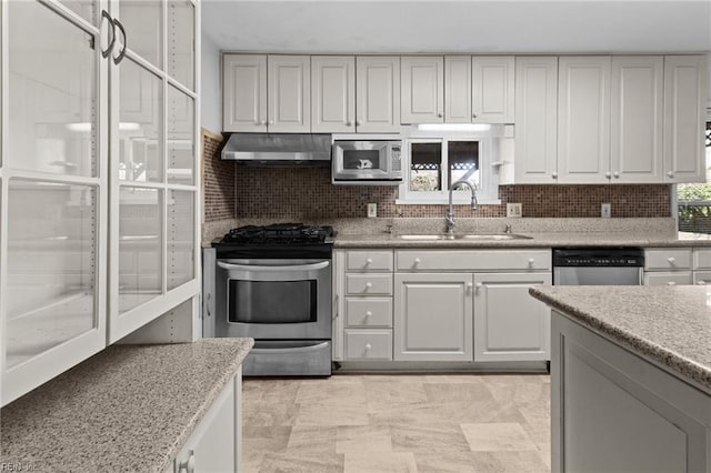 kitchen featuring light stone countertops, wall chimney range hood, backsplash, appliances with stainless steel finishes, and sink