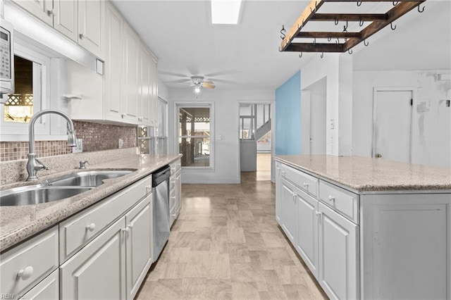 kitchen with dishwasher, ceiling fan, a kitchen island, sink, and white cabinetry