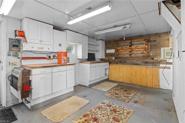 kitchen featuring white cabinets, heating unit, and wood walls