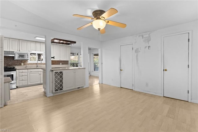 kitchen featuring stainless steel appliances, sink, ceiling fan, light wood-type flooring, and decorative backsplash