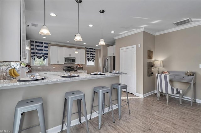 kitchen with decorative light fixtures, white cabinetry, a kitchen bar, light stone countertops, and appliances with stainless steel finishes