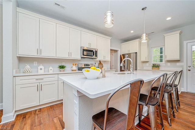 kitchen featuring stainless steel appliances, visible vents, a sink, an island with sink, and wood finished floors