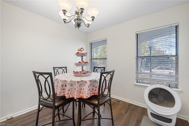 dining area with dark wood-type flooring and an inviting chandelier