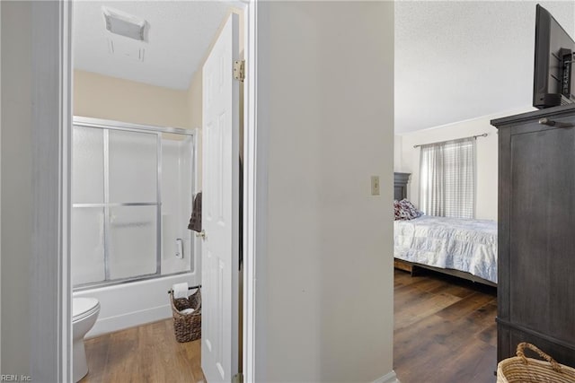 bathroom with toilet, enclosed tub / shower combo, and wood-type flooring