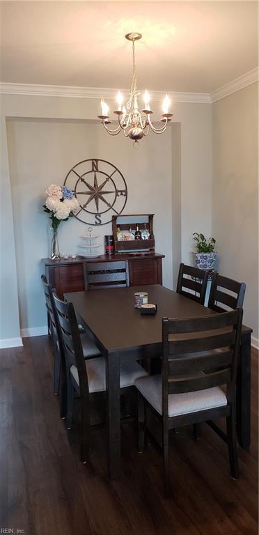 dining space with dark wood-type flooring, an inviting chandelier, and ornamental molding