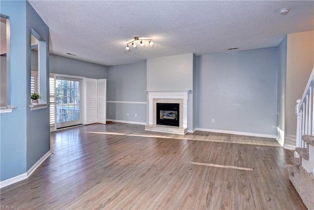 unfurnished living room featuring hardwood / wood-style flooring, a textured ceiling, and track lighting