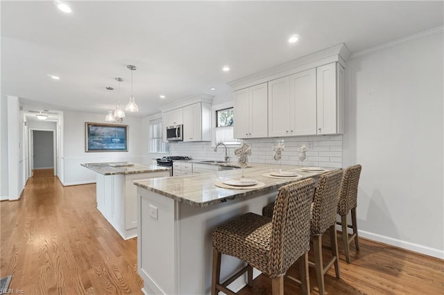 kitchen with white cabinetry, stainless steel appliances, light wood-type flooring, a kitchen island, and pendant lighting