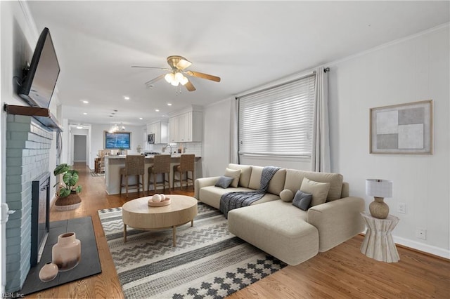 living room with ceiling fan, light hardwood / wood-style flooring, ornamental molding, and a fireplace