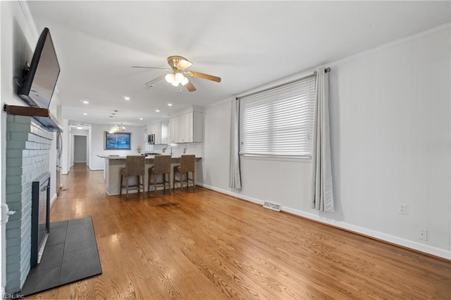 interior space with ceiling fan, a fireplace, a breakfast bar, kitchen peninsula, and white cabinets