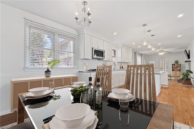 dining area with light wood-type flooring, sink, and ceiling fan with notable chandelier