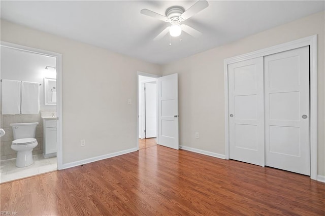 unfurnished bedroom with ensuite bathroom, ceiling fan, a closet, and hardwood / wood-style floors