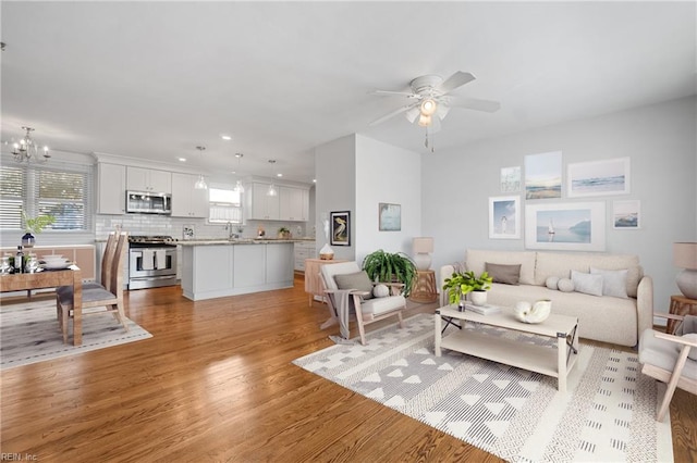 living room with light wood-type flooring, sink, and ceiling fan with notable chandelier