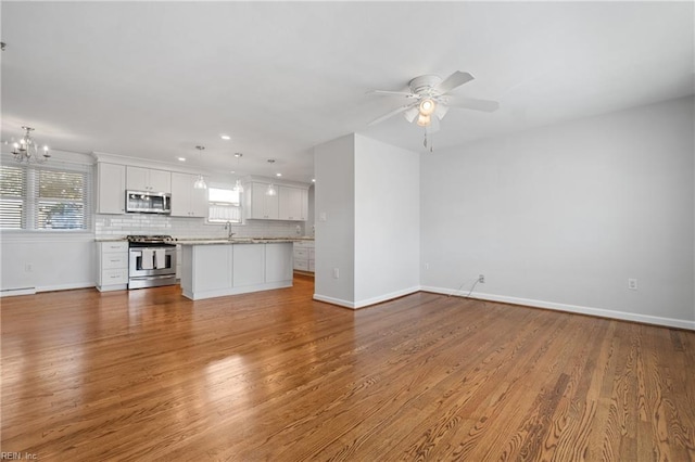 unfurnished living room with ceiling fan with notable chandelier, sink, wood-type flooring, and a baseboard radiator