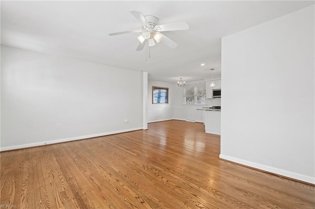 unfurnished living room featuring ceiling fan with notable chandelier and light hardwood / wood-style flooring