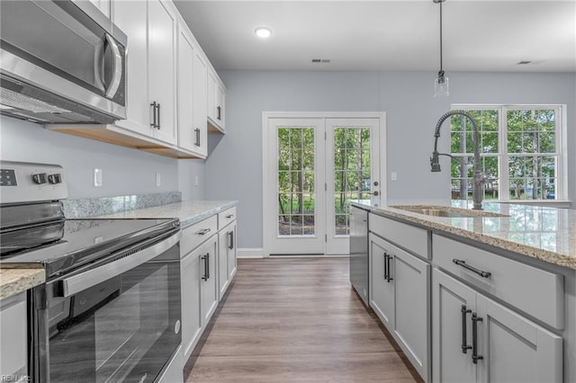 kitchen with light stone counters, decorative light fixtures, stainless steel appliances, white cabinets, and sink