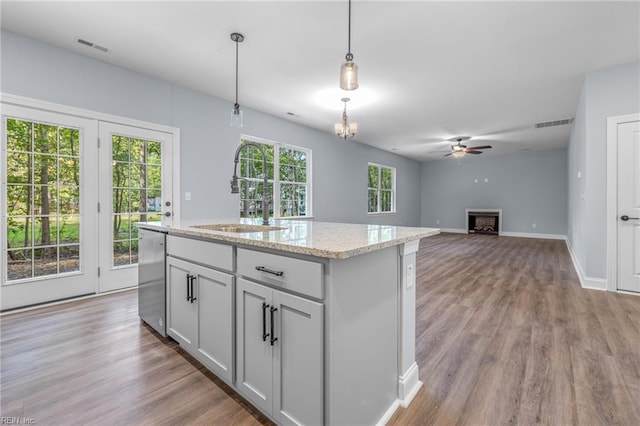 kitchen featuring hanging light fixtures, an island with sink, light stone counters, sink, and stainless steel dishwasher