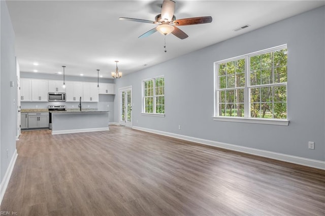 unfurnished living room featuring ceiling fan with notable chandelier, hardwood / wood-style flooring, sink, and plenty of natural light