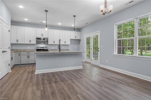 kitchen with stainless steel appliances, a kitchen island with sink, hanging light fixtures, and white cabinetry