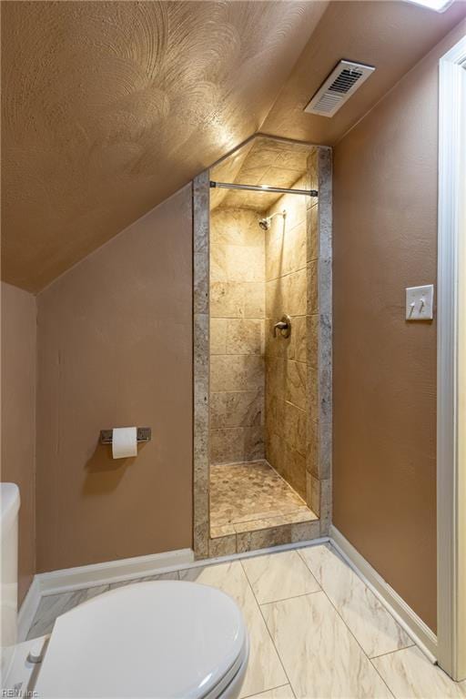 bathroom with toilet, tiled shower, and lofted ceiling