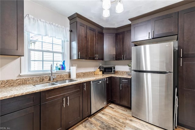 kitchen with appliances with stainless steel finishes, light wood-type flooring, light stone countertops, sink, and dark brown cabinets