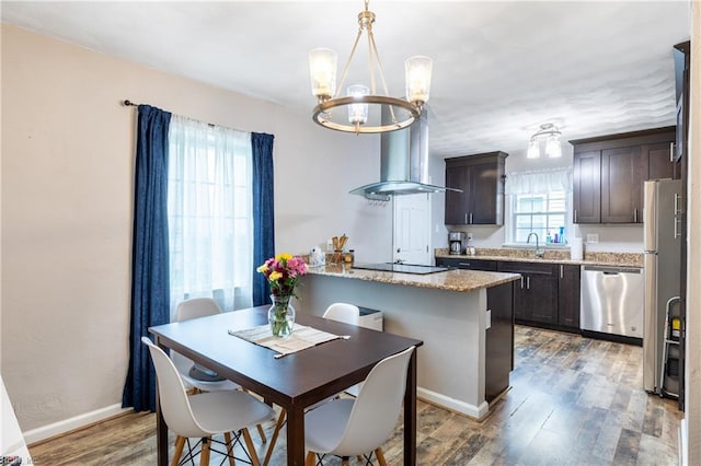 kitchen featuring wood-type flooring, appliances with stainless steel finishes, light stone counters, dark brown cabinets, and an inviting chandelier