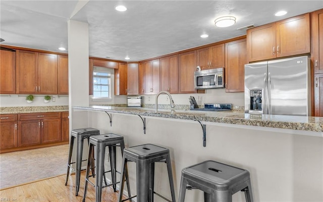 kitchen with light stone countertops, a kitchen bar, light wood-type flooring, appliances with stainless steel finishes, and sink