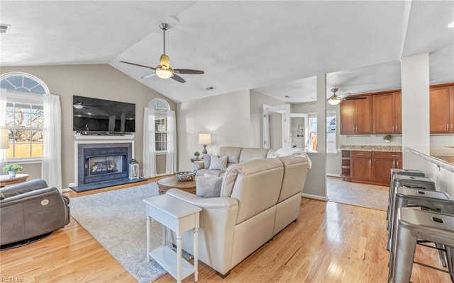 living room with ceiling fan, light wood-type flooring, a tile fireplace, and vaulted ceiling