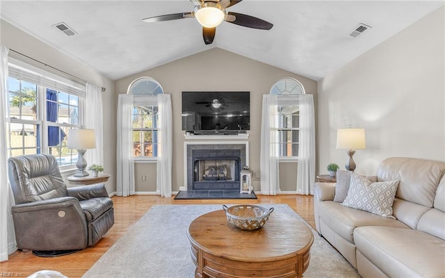 living room featuring a tile fireplace, ceiling fan, vaulted ceiling, and light hardwood / wood-style flooring