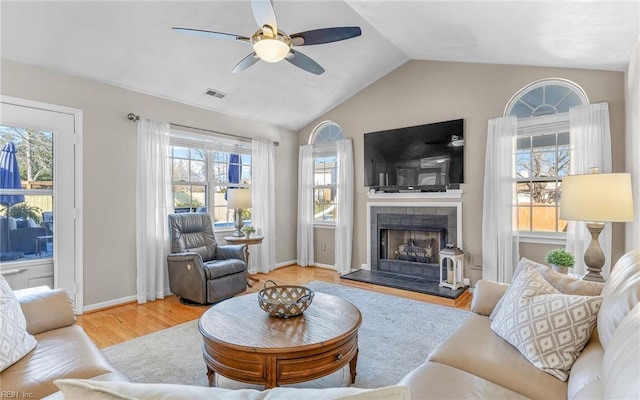 living room with ceiling fan, a tile fireplace, light wood-type flooring, and vaulted ceiling