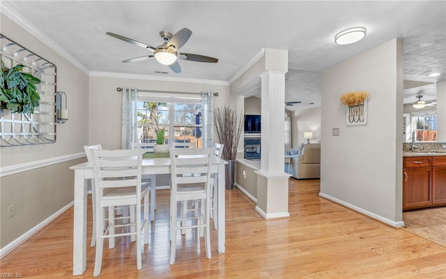 dining space with decorative columns, ceiling fan, crown molding, and light hardwood / wood-style flooring