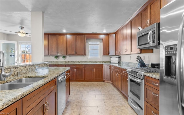 kitchen featuring appliances with stainless steel finishes, ceiling fan, light stone counters, and sink