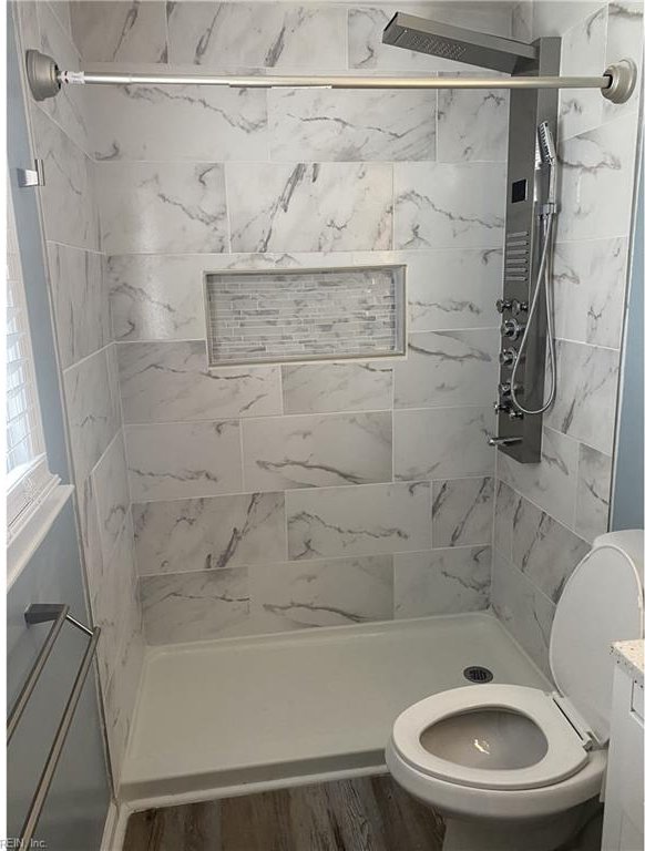 bathroom featuring hardwood / wood-style floors, a tile shower, toilet, and vanity