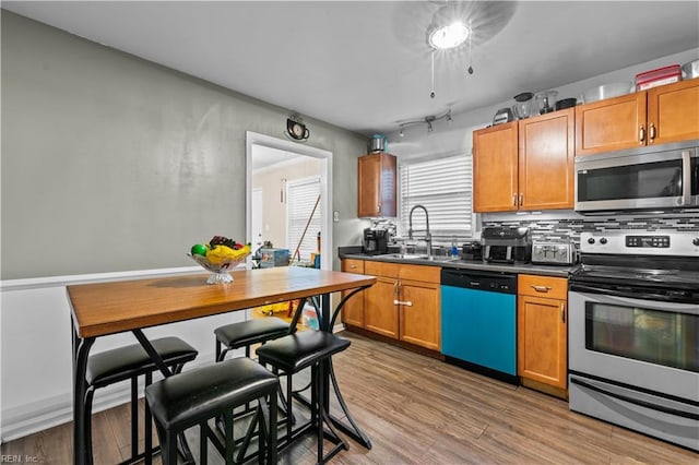 kitchen with appliances with stainless steel finishes, hardwood / wood-style floors, backsplash, and sink