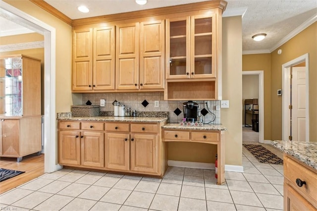 kitchen with light tile patterned flooring, ornamental molding, backsplash, and light stone countertops