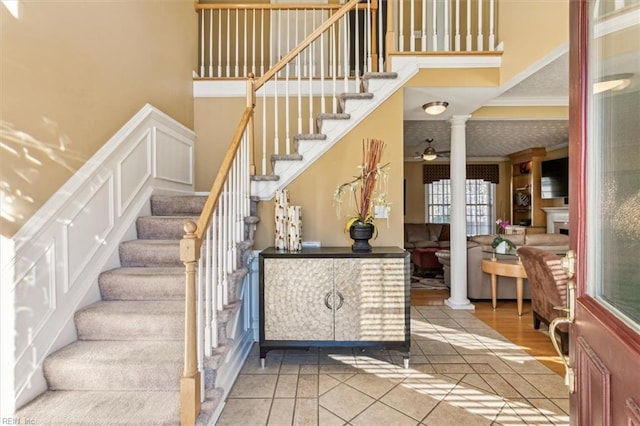 stairway with crown molding, decorative columns, ceiling fan, and tile patterned floors