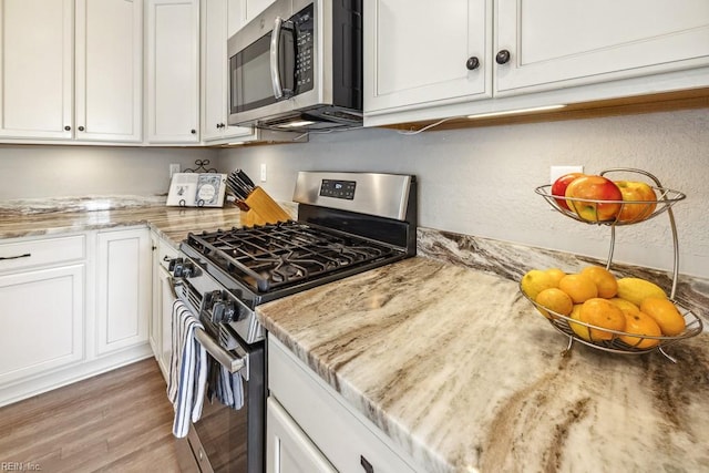 kitchen featuring light stone counters, stainless steel appliances, light hardwood / wood-style floors, and white cabinets