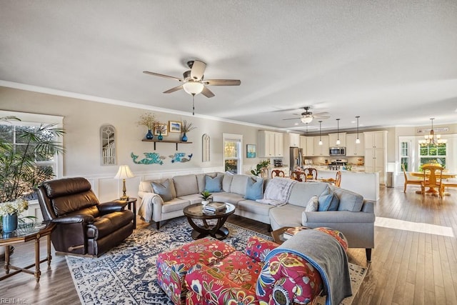 living room with ceiling fan with notable chandelier, a textured ceiling, crown molding, and hardwood / wood-style floors