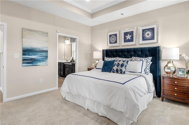 carpeted bedroom featuring ensuite bath, ornamental molding, and a tray ceiling