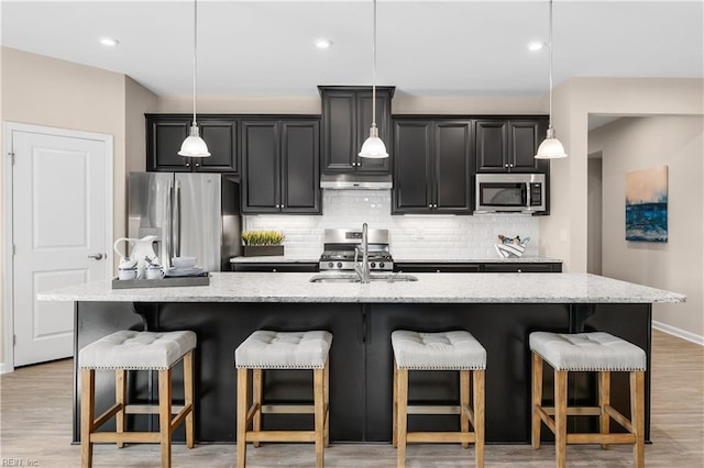 kitchen featuring stainless steel appliances, decorative light fixtures, a breakfast bar, and an island with sink