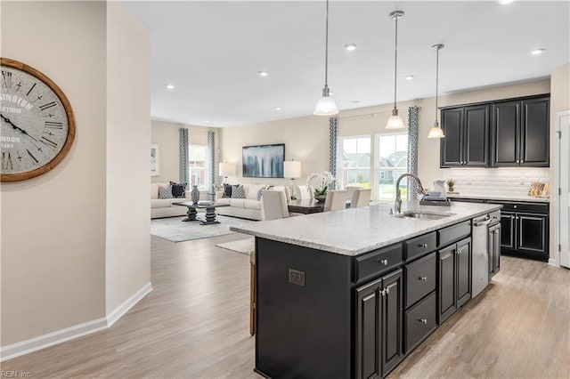 kitchen with sink, a center island with sink, light wood-type flooring, and pendant lighting