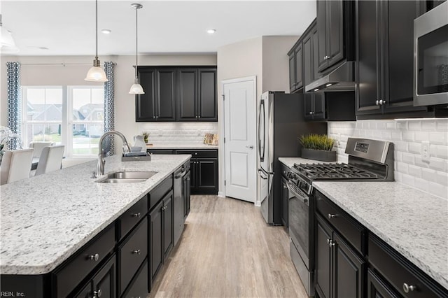 kitchen featuring appliances with stainless steel finishes, hanging light fixtures, an island with sink, decorative backsplash, and sink