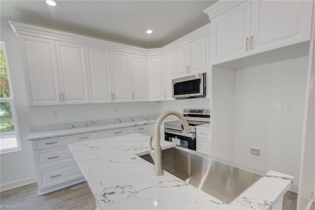 kitchen featuring light wood-type flooring, light stone countertops, stainless steel appliances, and white cabinetry