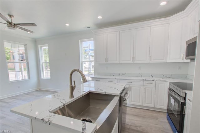 kitchen with white cabinets, appliances with stainless steel finishes, an island with sink, and light stone counters