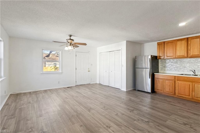 kitchen featuring sink, ceiling fan, light hardwood / wood-style floors, tasteful backsplash, and stainless steel fridge