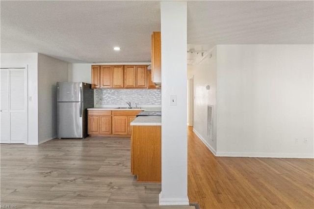 kitchen with sink, decorative backsplash, stainless steel refrigerator, and light wood-type flooring