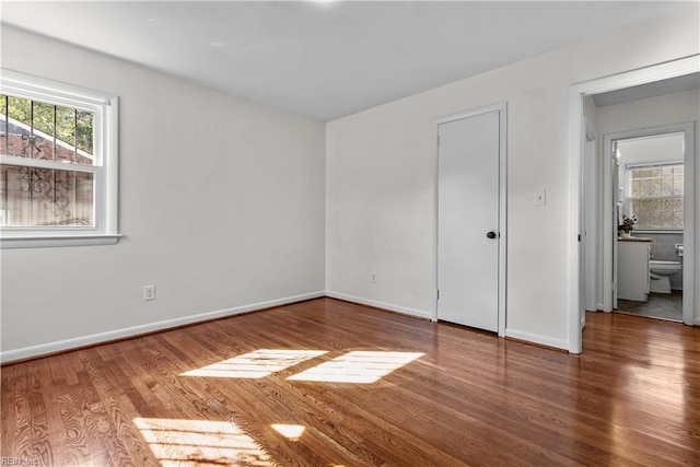 unfurnished bedroom with ensuite bathroom and hardwood / wood-style floors