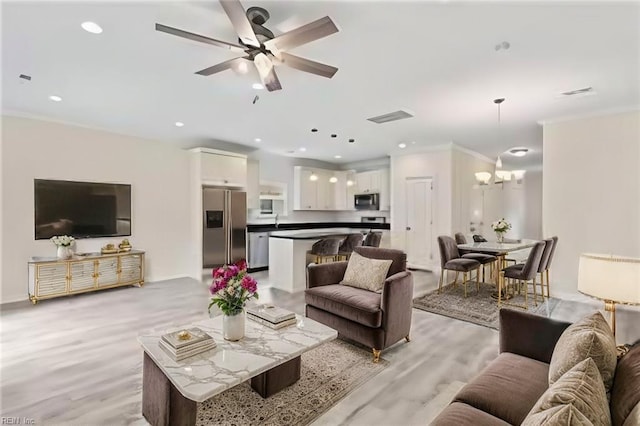 living room with ceiling fan with notable chandelier, light hardwood / wood-style floors, crown molding, and sink