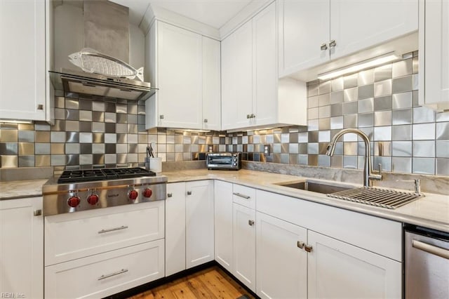 kitchen featuring appliances with stainless steel finishes, sink, white cabinetry, wall chimney range hood, and tasteful backsplash